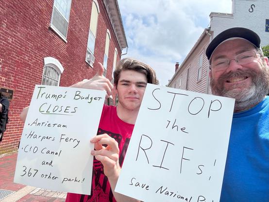 Two men holding rectangular signs.  One reads "Stop the RIFs - Save National Parks" the other reads "Trump's Budget closes Antietam, Harpers Ferry, C&O Canal, and 367 other parks"
