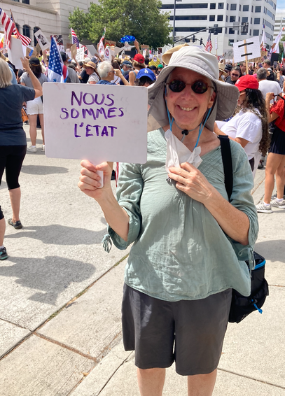 me wearing a gray gardening hat. sunglasses. Mask lowered. Holding a sign Nous Sommes L'Etat.