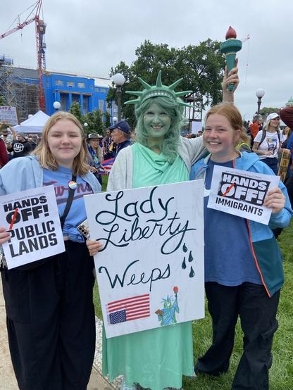 Protesters with signs: HANDS OFF! PUBLIC LANDS 

Lady Liberty Weeps (held by a person in Statue of Liberty costume)

 HANDS OFF! IMMIGRANTS