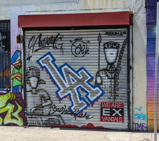 roll down gate with graffiti and a sign saying we are ex vandals