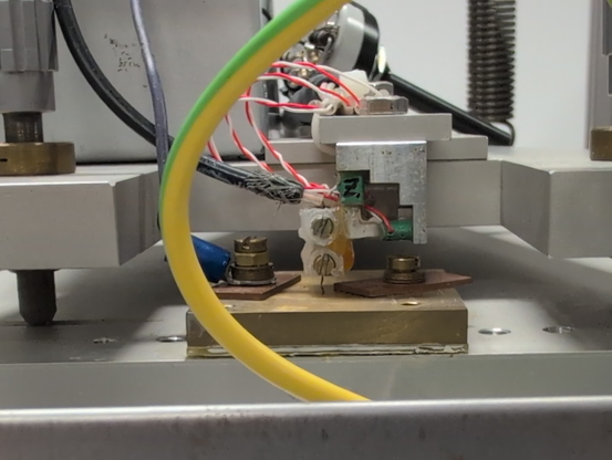A tungsten probe in some hot glued holder, attached with piezo crystals to an aluminium frame. Tension springs in the background form part of a dampening system.
