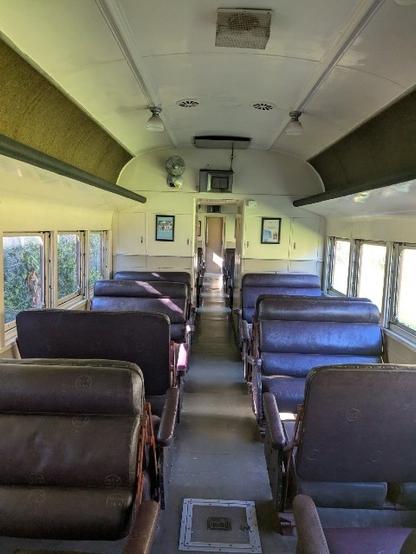 The inside of an old train showing 2 rows of brown leather double seats.