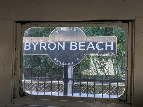 The Byron Beach train station sign, framed by a train window.