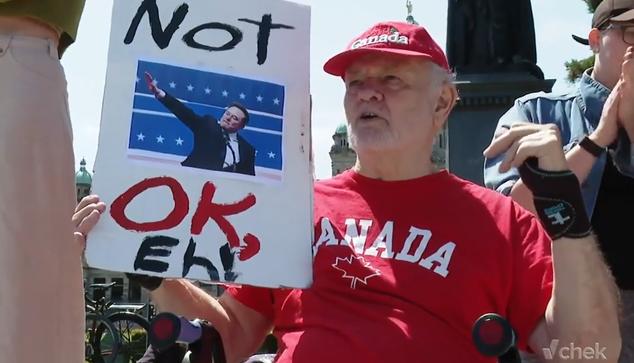 Older man sitting on walker holding a sign of Elon Musk doing a Nazi salute "Not OK, Eh". He is wearing a red Canada shirt and hat.