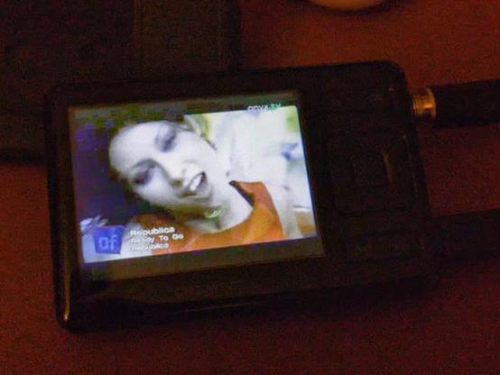 A poorly lit photograph of a Creative Zen mp3 player, a device about the width of a modern smartphone but a third of the size with a tiny 2.5inch (65mm) TFT LCD screen playing video at a surprisingly watchable 320 by 240 resolution. The screen is showing the video for Ready To Go by Republica.