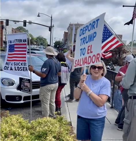 A third angle of the crowd protesting for No Kings Day, June 24, 2025, in front of the Marshall County Courthouse in Guntersville, Alabama.  One person holds a sign that, above and below an American Flag, reads:
"I'M A VETERAN
NOT A SUCKER
OR A LOSER"

And another that reads: "DEPORT TRUMP TO EL SALVADOR"