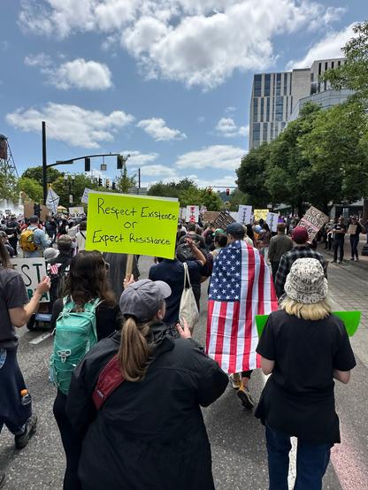 Large crowd marching along the Portland waterfront. One visible sign reads "Respect Existence or Expect Resistance"