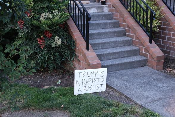 A handwritten sign with a political message is placed on the ground near a brick staircase outside a building.