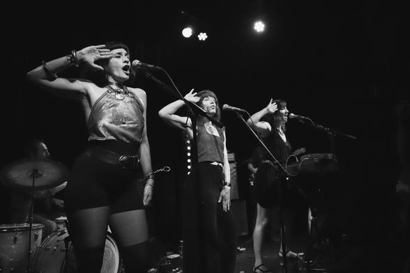 Une photo noir et blanc de Marie-Louise, Wendy et Amy, les trois chanteuses du groupe Gloria, en pleine chorégraphie un rien moqueuse pendant un concert du groupe au Périscope à Lyon, le 12 juin 2025.