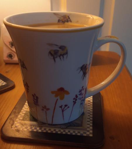 A summery mug of tea on a bedside cabinet with flowers and bees