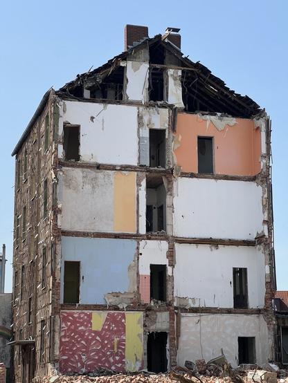 A photo of a half-demolished house: The building is still intact in its height but has been opened vertically so that the walls of the individual residential units, painted in different colours, and the door openings can be seen. 

Photo credits: me