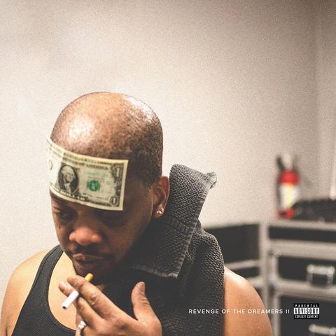 Album Revenge Of The Dreamers II avec en bas à gauche de la photo un homme noir moustachu et barbu qui s'apprête à fumer, 1 dollar collé sur le front et un serviette gris foncé sur l'épaule gauche, dans un décor vide, terne et flou