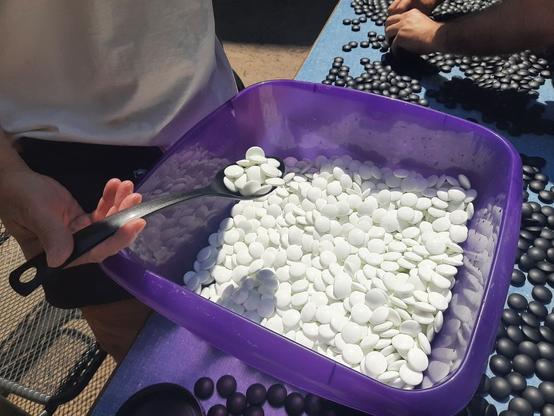 approximately 1500 white go stones in a plastic tub and a similar amount of black stones laid out on a table in the sun to dry. don't do it like this though - place the stones on a towel.