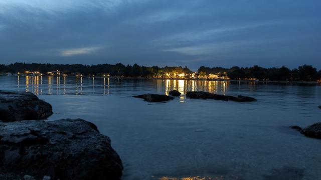 Blick aufs Meer in einer Bucht zur gegenüberliegende Seite das beleuchtet ist, aus der Meeresoberfläche ragen ein paar Steine heraus