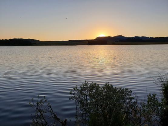 Vue sur le lac de Bourdouze en Auvergne, au soleil couchant derrière les collines à l'horizon.