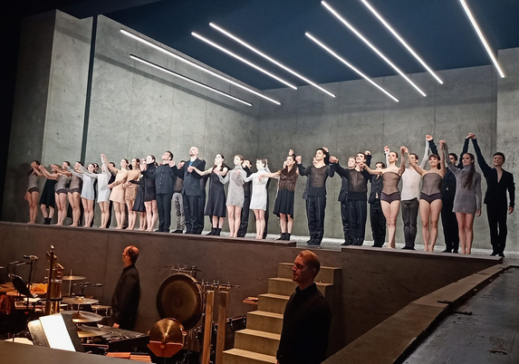 Das Ballett, der Sänger und der Dirigent verbeugen sich. Im Vordergrund sieht man im Graben zwei Musiker