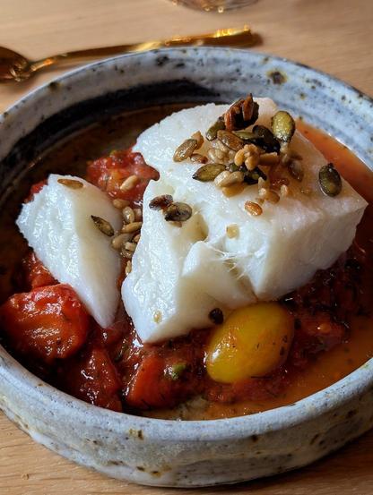 Salt fish with roasted crispy seeds on top all sitting in a red tomato sauce