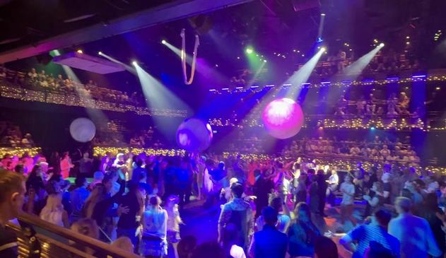 The centre of the theatre in the round with the “immersive standing” audience playing with huge inflatable balls. The lighting is green, blue, purple and pink.