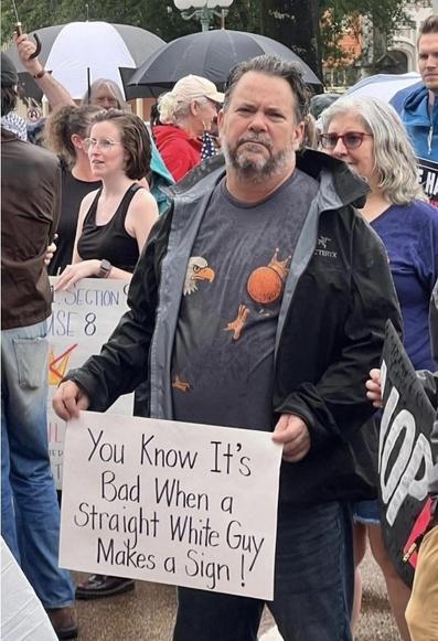 Middle aged, average looking white man, holding a sign that says “You know it’s bad when a straight white guy makes a sign!”