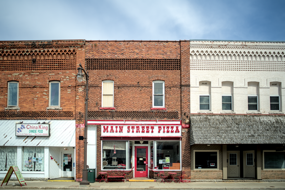Manistique Main Street storefronts – A row of vintage brick buildings including “China King” and “Main Street Pizza,” with red awnings, tables on the sidewalk, and classic early‑20th‑century storefront charm.