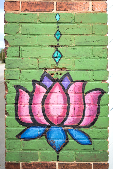 Painted lotus mural on brick pillar – A vertical green-painted brick column features a stylized pink and blue lotus flower with teal diamond accents.