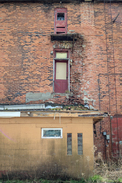 Red door in weathered brick – Two stacked red-painted doors (one upper-level with no balcony) set into a worn red brick wall above a mustard-yellow exterior.