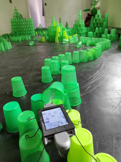 An installation all made of green plastic cups, forming alignments all through the room interconnecting "buildings" made of stacked green cups. The DigtalBug is posted at the junction of two lines with a different tint of green.