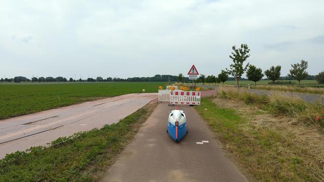 Ein Velomobil steht vor Absperrbaken auf dem Radweg von Sülldorf nach Bahrendorf. Ein Schild sagt Achtung, Radfahrer absteigen.