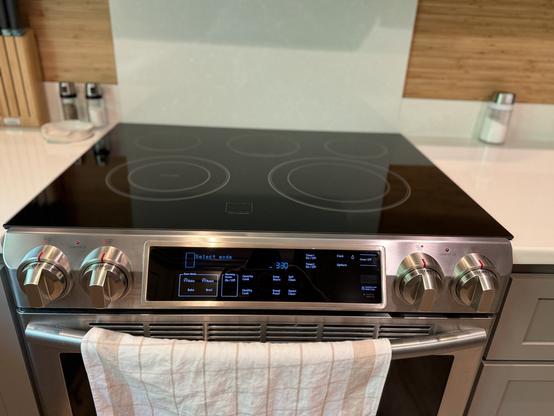 Modern stainless steel stove with a sleek glass top and digital controls. A white kitchen towel hangs on the oven handle, creating a clean, contemporary look.