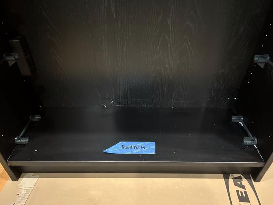 Interior shot of IKEA BILLY bookcase showing silicone crumbs stuck to the back wall.  A piece of blue painter's tape is taped to the shelf, labeled "BOTTOM".