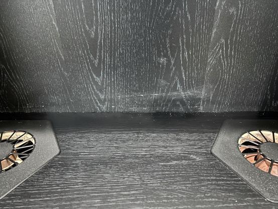 An interior shot of the IKEA BILLY bookcase showing dried silicone smeared on the back wall above a shelf.  The shelf is caulked to the back.  There are two vent holes on opposite ends of the shelf, and the right one has a fan in it.