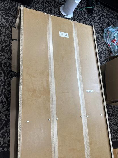 The back side of an IKEA BILLY bookcase lying on the floor.  The back surface is particle board with thickly brushed on polyurethane sealant.  There are silicone caulk beads running along the left and right edges.