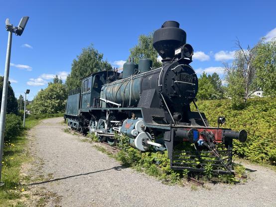 Front and side Picture of An old steam engine in a park. It is painted blue all over but the first meter which is black.