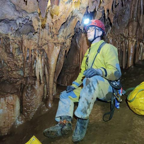 A person sitting in a cave, their headlight illuminating dripstones