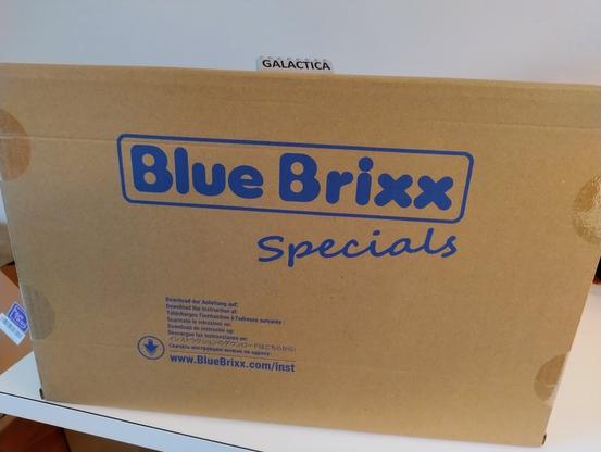 Großer Karton mit der Aufschrift "Blue Brixx". Auf dem Karton ein bedruckter Klemmbaustein mit der Aufschrift "GALACTICA"