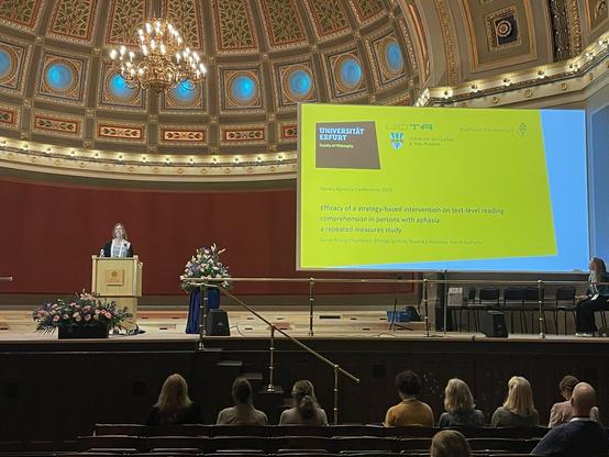 This image shows Dr Thumbeck at the conference next to the slides also listing the co-authors of the study P. Schmid, S. Chesenau and F. Domahs.