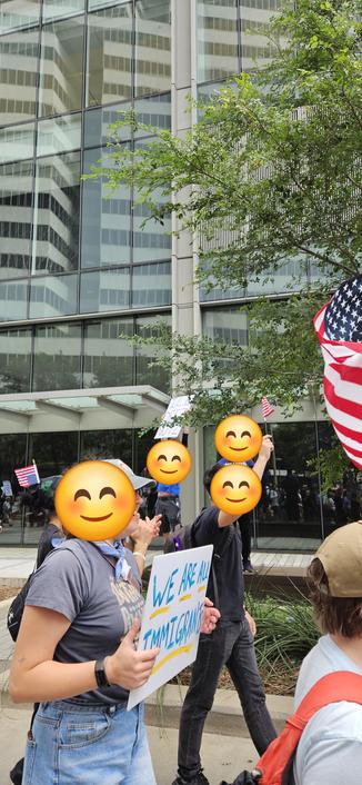 A person standing on a bench on a sidewalk holds a sign that reads, "ICE DEEZ NUTZ."