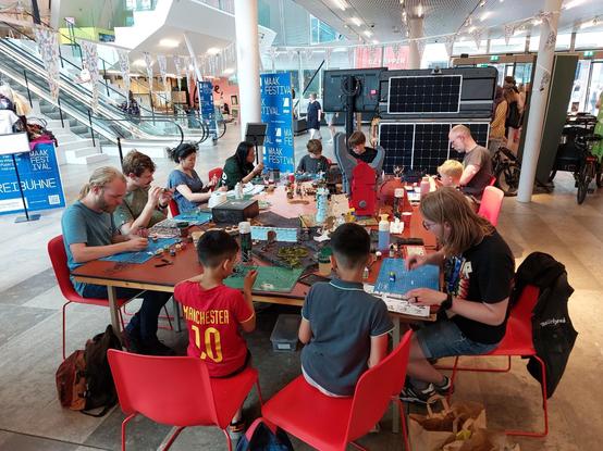 Massive table in a very modern library with a variety of people of ages and backgrounds sat hobbying.