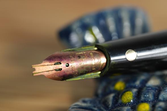 Closeup of a three-tine nib with a gap in the middle tine. Nib has purple ink on the nib. Nib is engraved "Osmiroid SH4 ENGLAND"