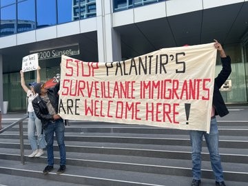 Protesters holding a massive banner reading STOP PALANTIR'S SURVEILLANCE IMMIGRANTS ARE WELCOME HERE