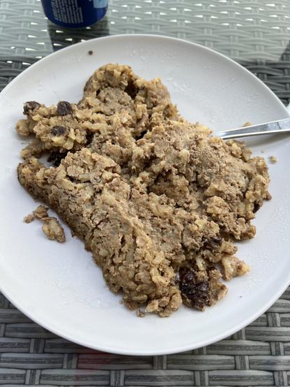 A brown mass on a plate with white spots and raisins and a spoon.