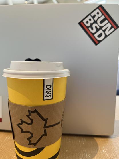 Photo of a laptop with a “Run BSD” sticker and a yellow coffee cup with a maple leaf