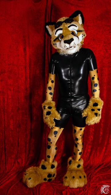 Photo of Obscura in fursuit partial, and wearing a cheetah print spandex bodysuit and black latex surfsuit