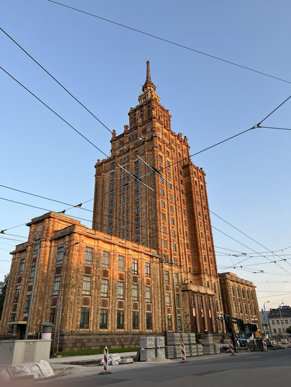 The Latvian academy of sciences, a tiered tower structure that has been turned golden by the sunset with clear blue sky in the background