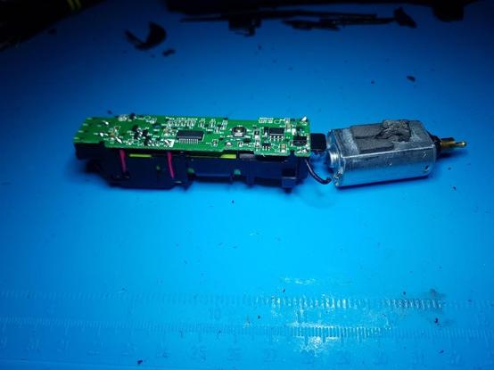 Une carte électronique et un moteur d'une tondeuse à barbe. On voit un fil coupé qui aliment le moteur.