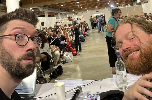 Nos deux têtes de glandus devant l’assistance de la table ronde à laquelle on a participé au congrès. En arrière plan un bibliothécaire inspiré photobomb avec le signe universel des deux doigts coupe-faim.