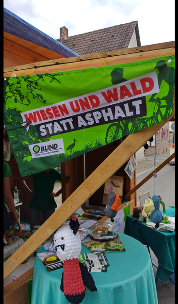 Ein Marktstand des BUND Langen-Egelsbach mit einem Banner "Wiesen und Wald statt Asphalt", verschiedenen Infomaterial und gehäkelten Fledermäusen.
