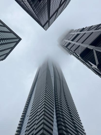 Four skyscrapers disappear into a low fog. Image is grey and misty.