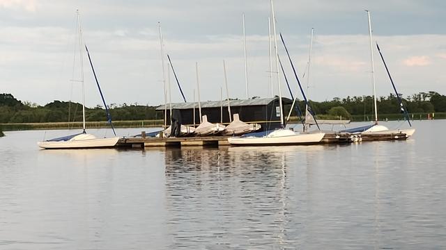 A cluster of Yeoman dinghies moored by or found on a pontoon in the middle of Barton Broad.