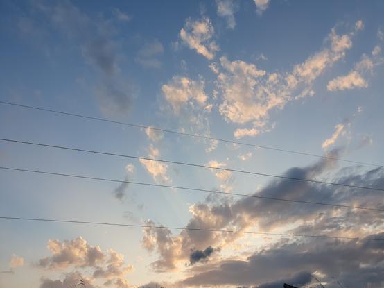 Photo d'un ciel au moment du soleil couchant (non visible), avec des rayons de lumière qui traversent des nuages de diverses couleur entre le jaune doré et le gris sombre